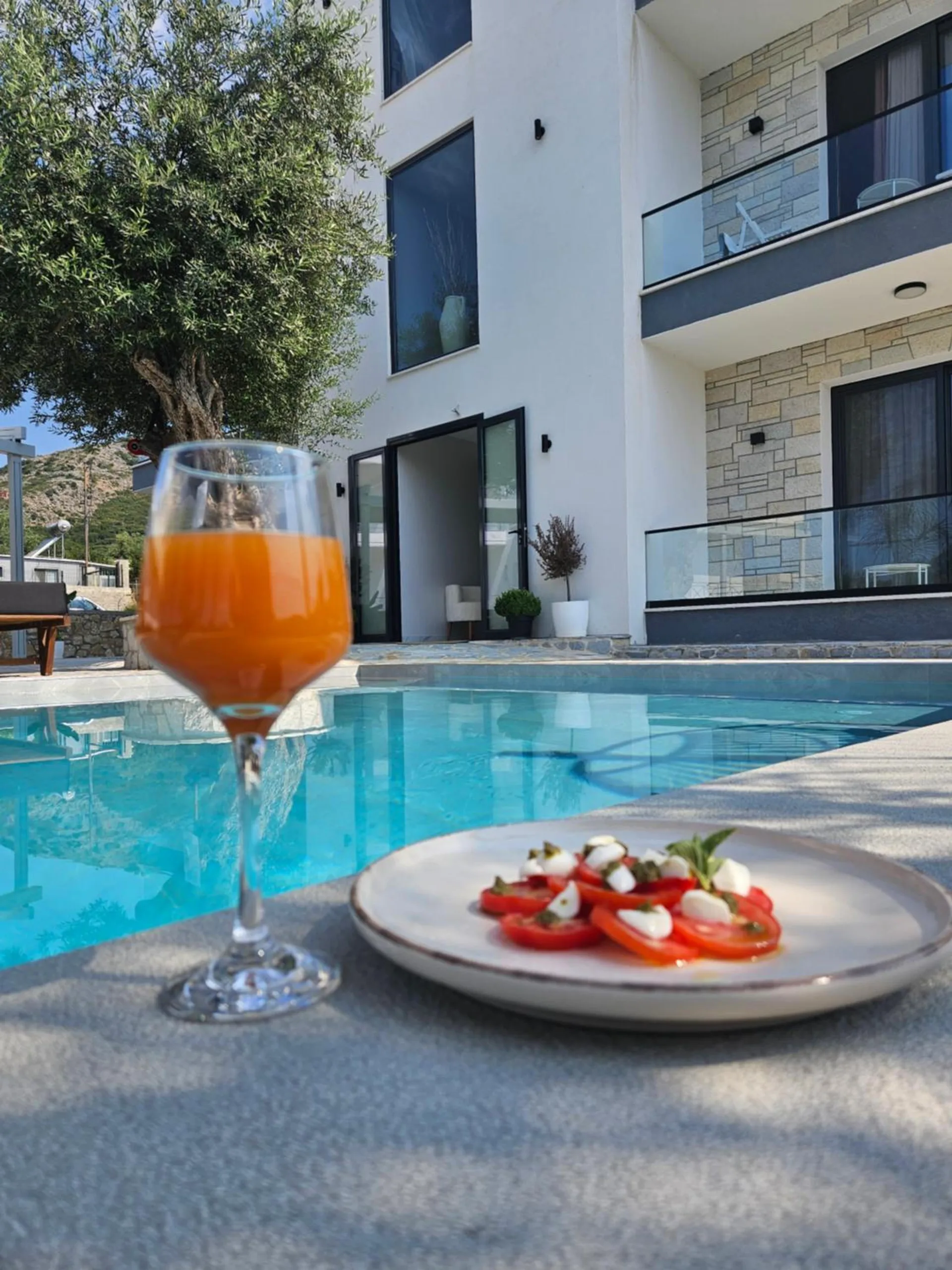 A glass of orange juice and a plate of tomato and mozzarella on the pool's edge, the house behind