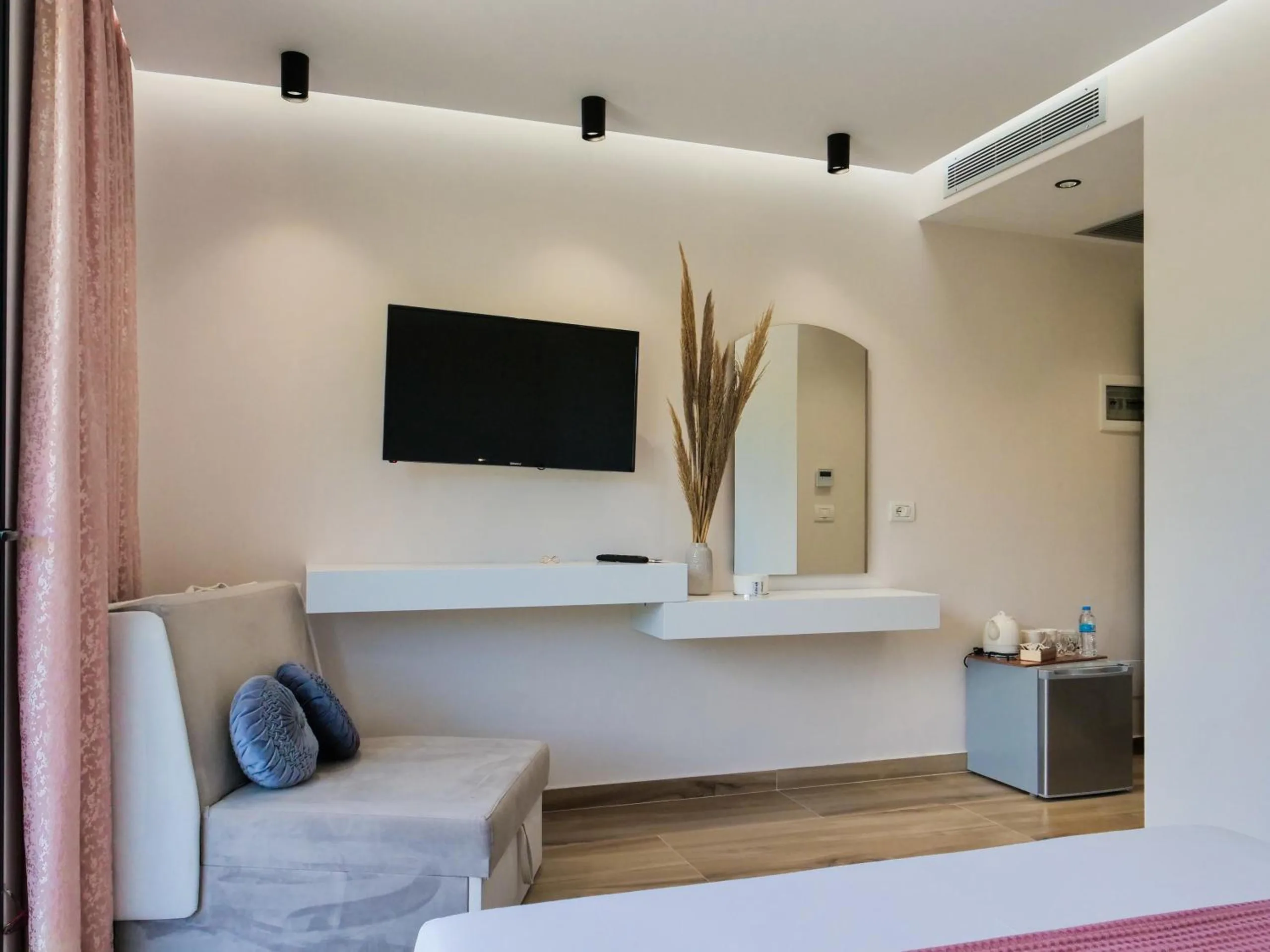 A sitting corner with a grey sofa, a wall-mounted television, a floating white shelf and a vase of pampas grass