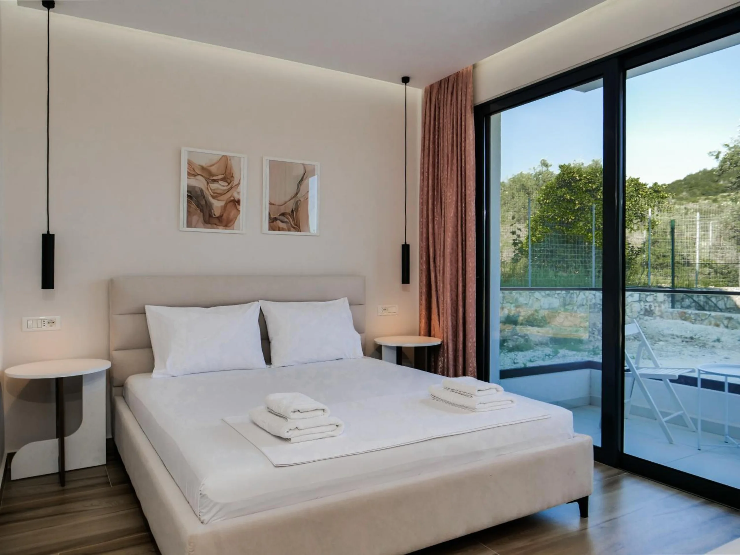 A double bed under two framed prints, rose curtains and glass doors onto a terrace with olive trees outside