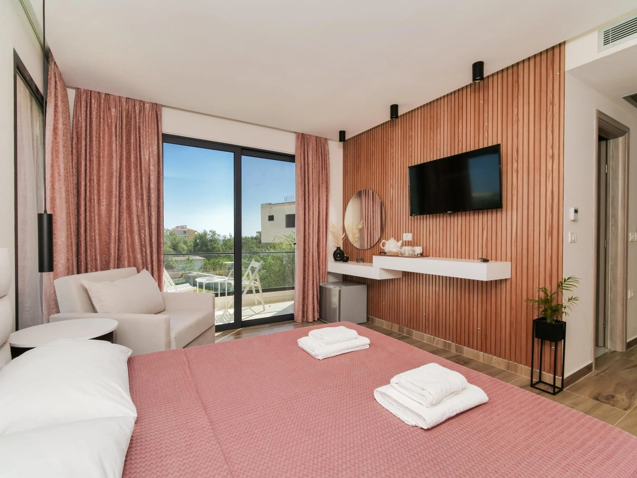 A room with a walnut slat wall behind the television, rose curtains at the glass doors and an armchair