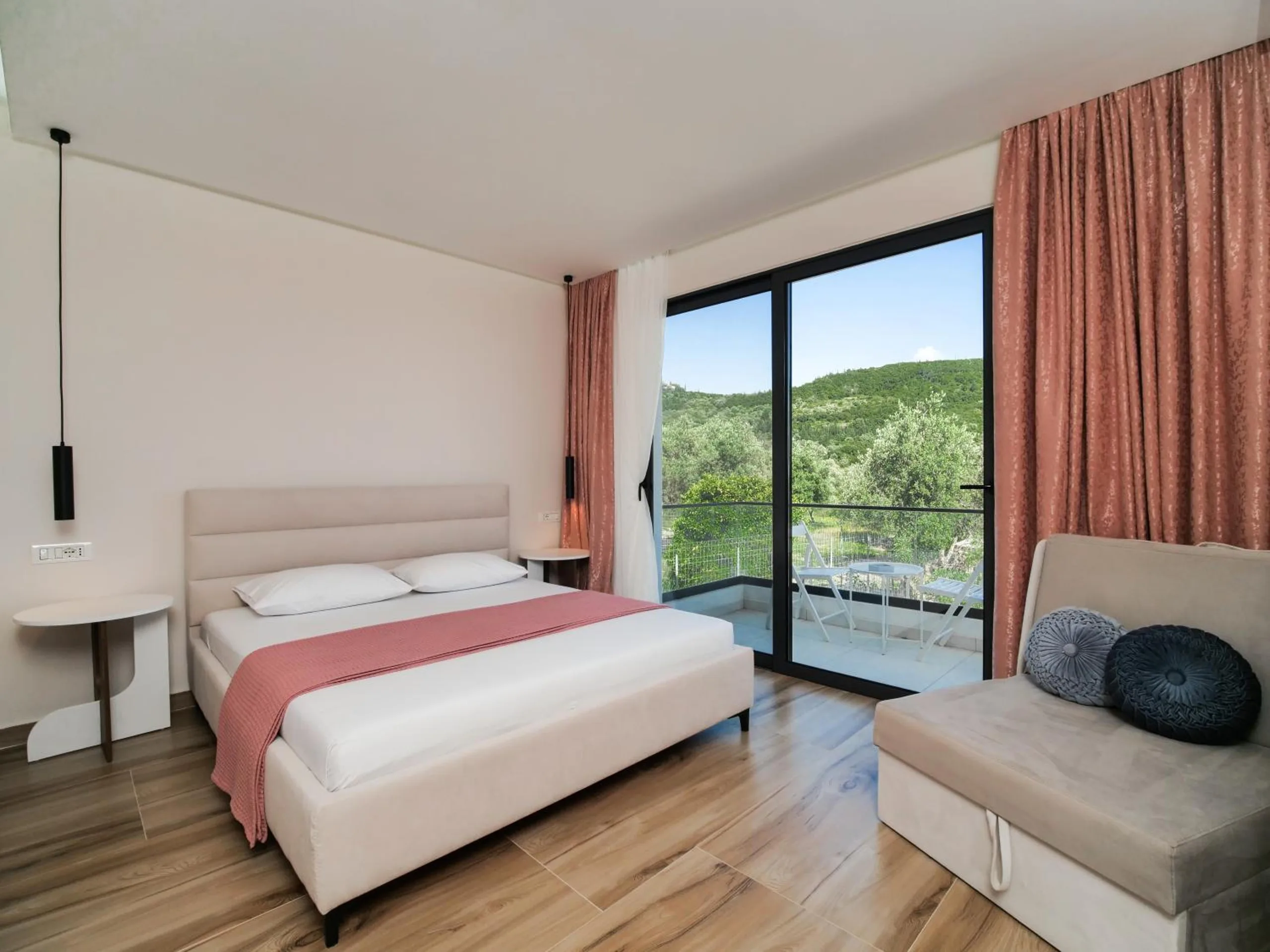 A double bed with a rose runner, a grey sofa with two cushions and glass doors to a green hillside