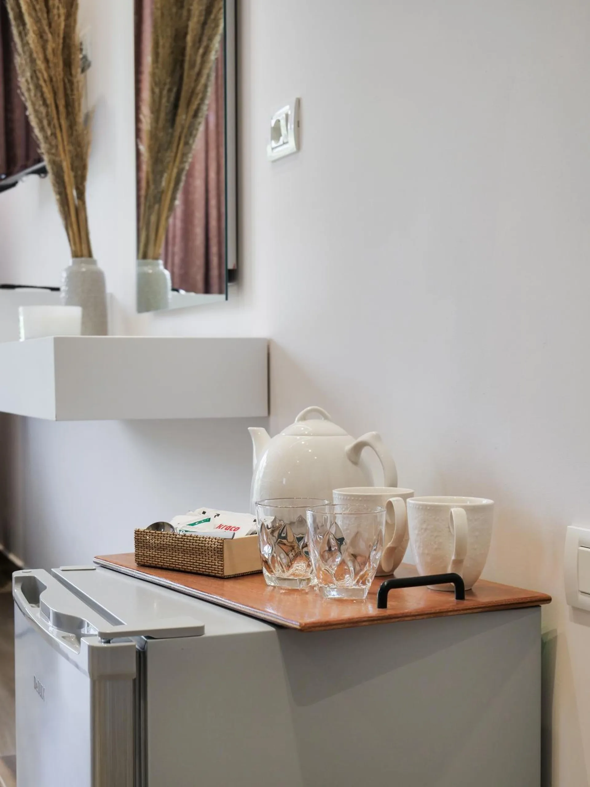 A white kettle, glasses and a tray of tea and coffee on top of a small fridge