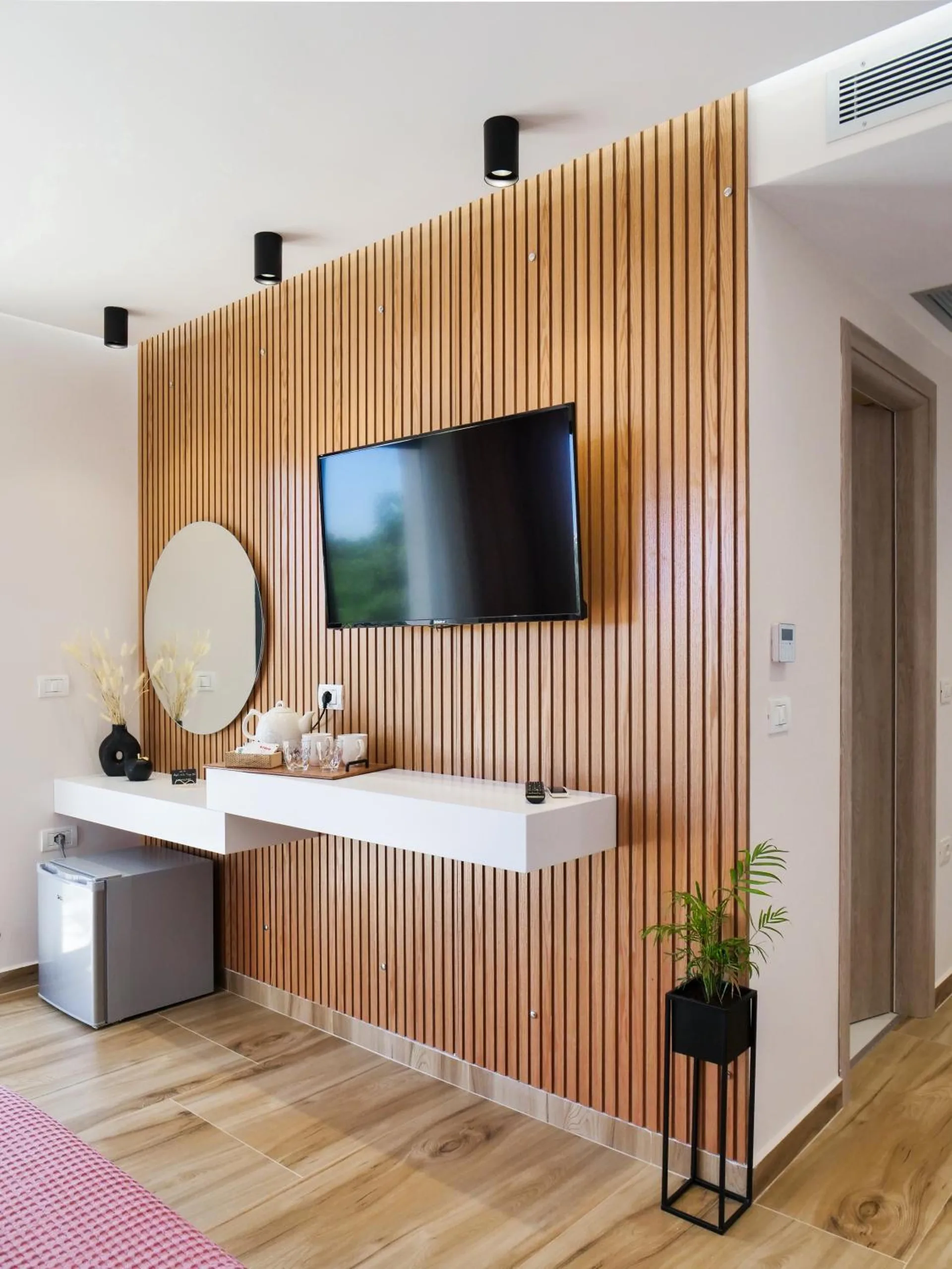 A floating white desk with a round mirror, a kettle and a small fridge in front of a walnut slat wall